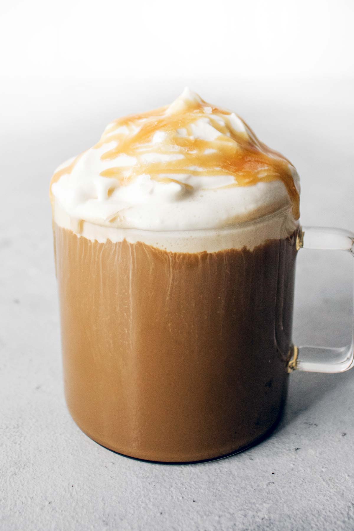 Gezouten karamel latte gegarneerd met slagroom en karamel besprenkeling in een glazen mok.