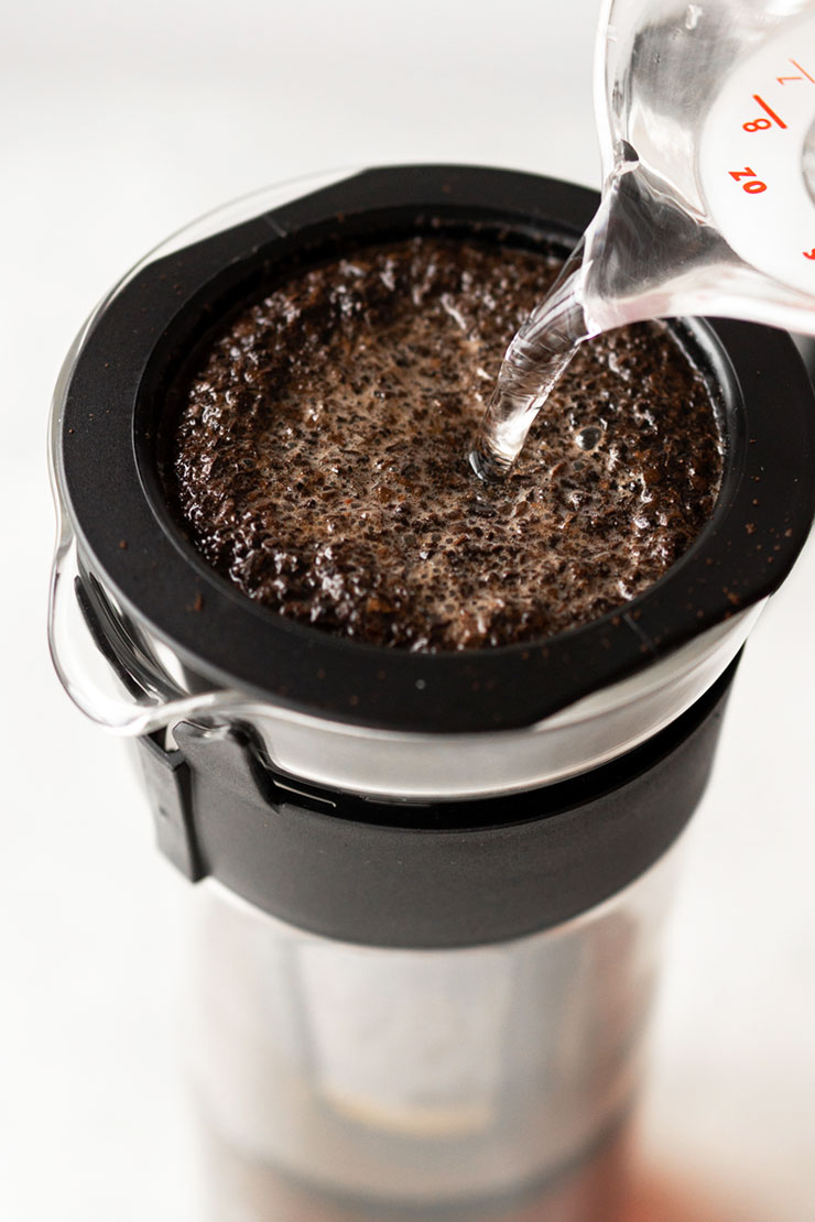 Giet water over gemalen koffie in een cold brew maker.