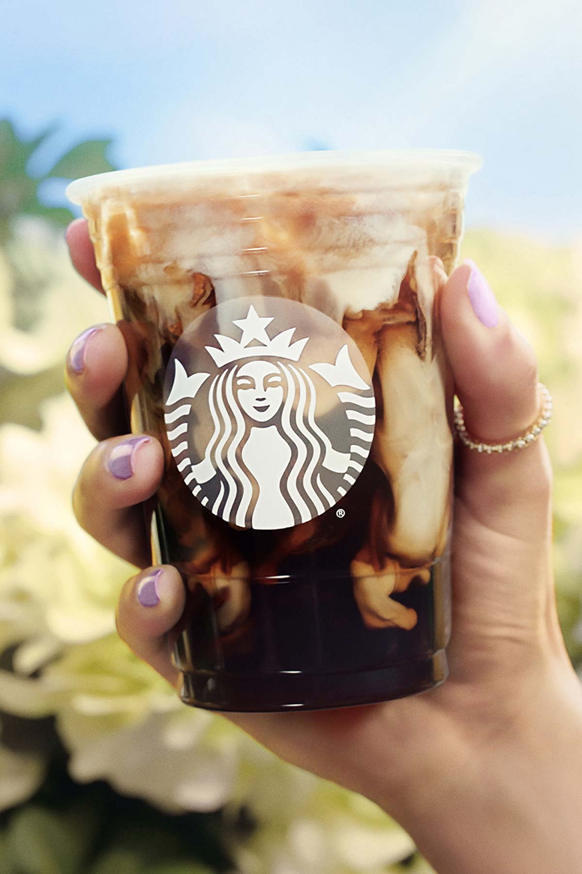 Hand met een Iced Toasted Vanilla Oatmilk Shaken Espresso in een Starbucks-kopje.