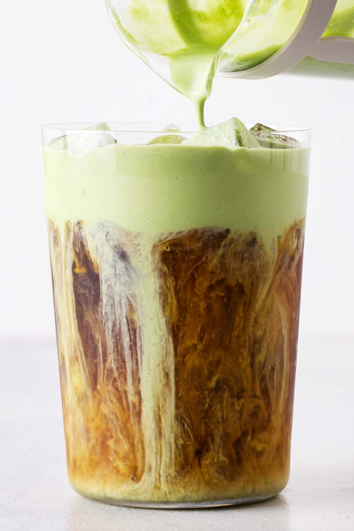 Matcha koudschuim wordt over een ijskoffie in een hoog glas gegoten.